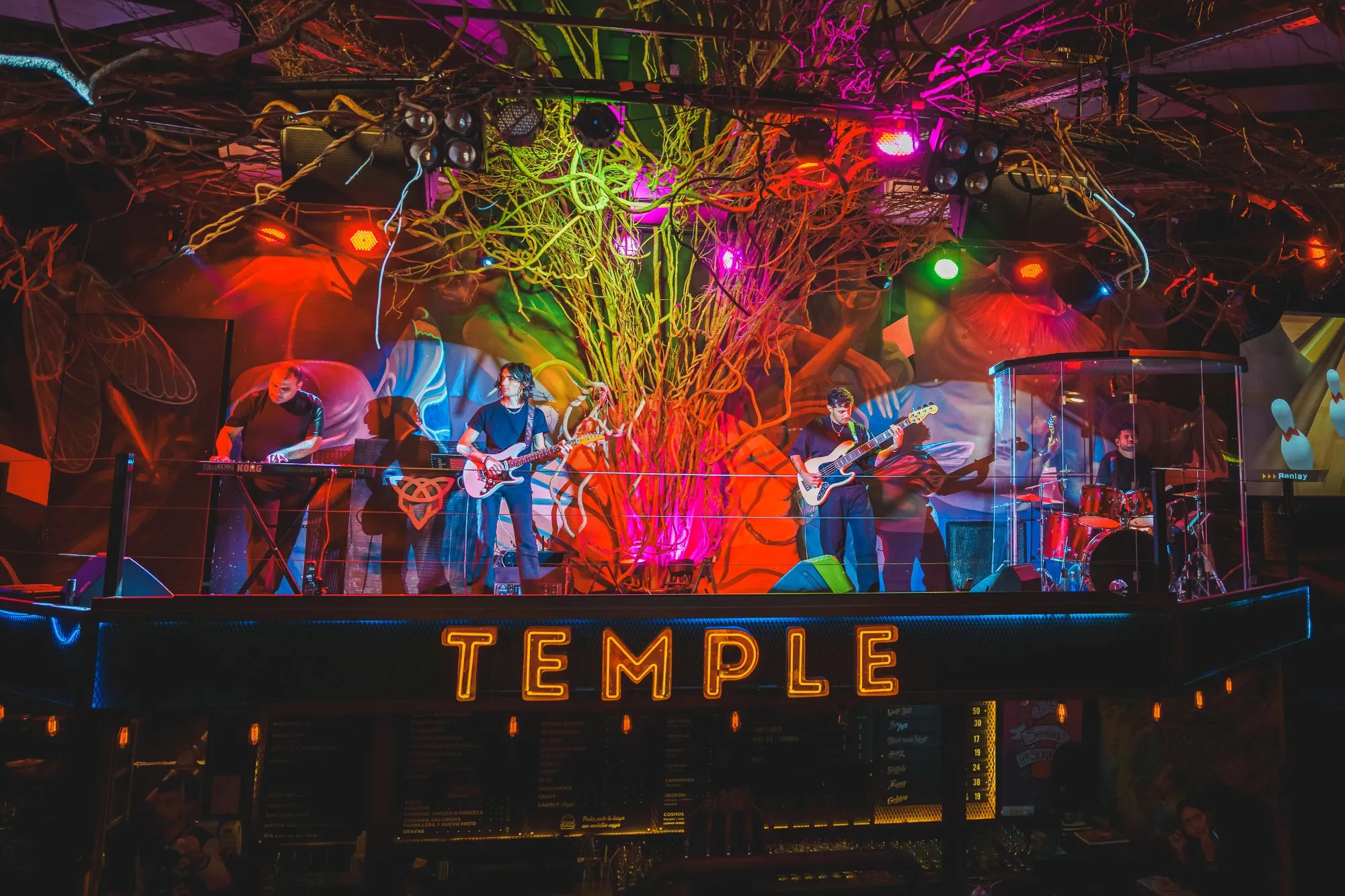 The Fandom Band tocando en el escenario de Club Temple, con luces de colores y el cartel de neón TEMPLE